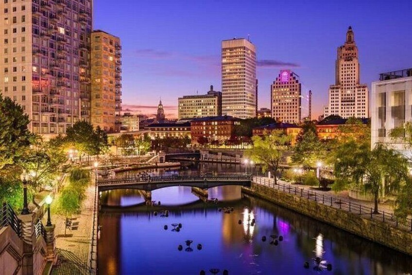 A cityscape at dusk with illuminated buildings, a river, and a bridge. 3