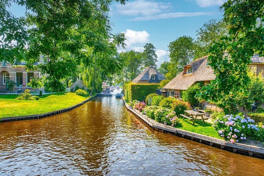 A canal with houses on one side and a grassy area with flowers on the other. 4