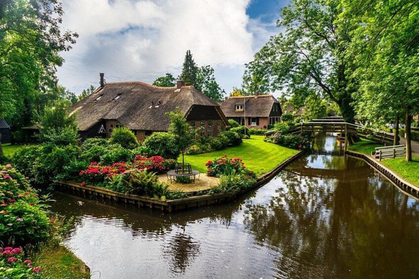 A canal with a house and garden, a wooden bridge, and lush greenery. 2
