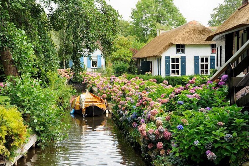 A narrow canal with a boat, lush greenery, and traditional houses. 3