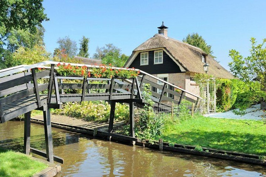 A wooden bridge over a canal, a thatched-roof house, and lush greenery. 5