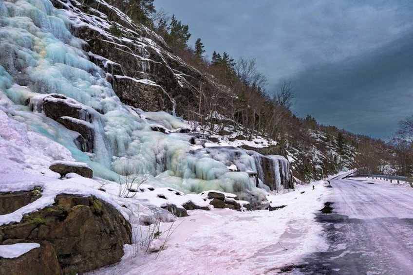A frozen waterfall with snow-covered rocks and a road. 4