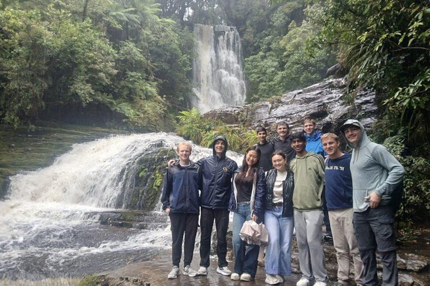 A group of people standing in front of a waterfall in a forested area. 4
