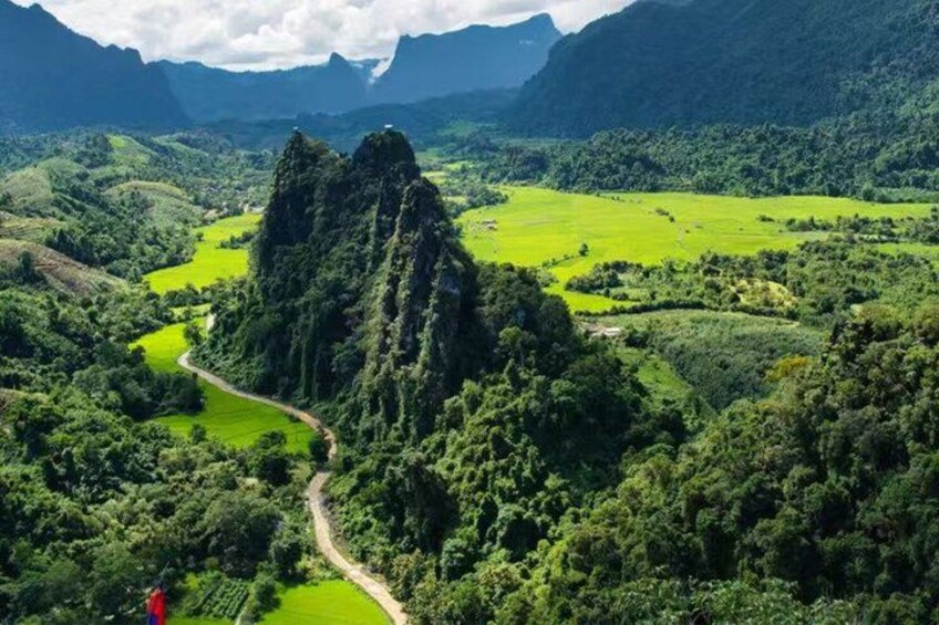 A mountainous landscape with a prominent rocky peak, lush green fields, and a winding road. 3