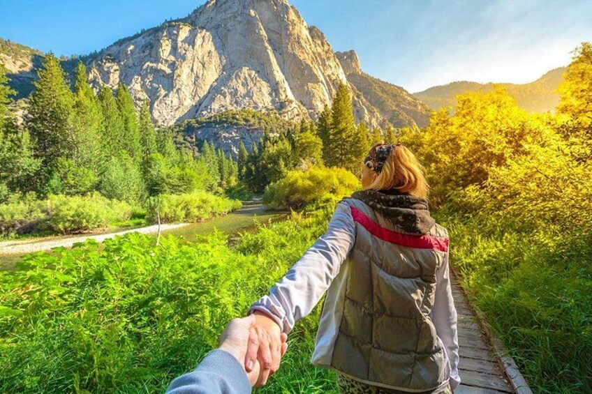 A person holding hands with another person walking on a wooden path through a green landscape with a mountain in the background. 3