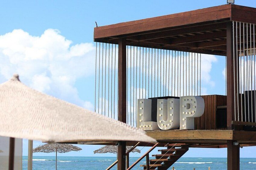 Una sombrilla de playa, una estructura de madera con la palabra 'LUP' y vista al océano. 1