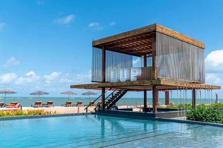 Una estructura de madera con una piscina al frente y sombrillas de playa al fondo. 5