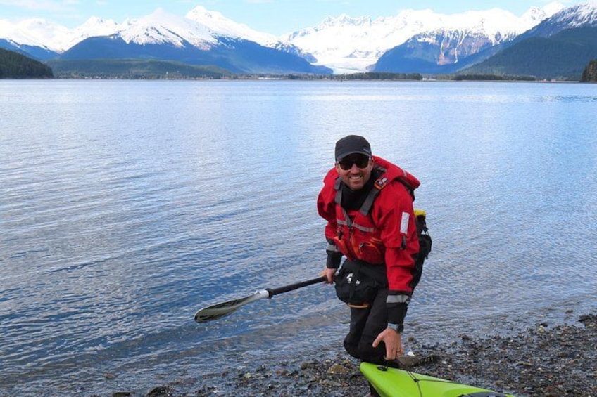 Una persona con chaleco rojo rema en kayak sobre un lago tranquilo, con montañas al fondo. 3
