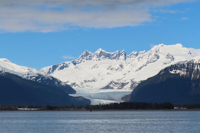 Un glaciar entre montañas nevadas, un lago tranquilo y un cielo despejado. 2