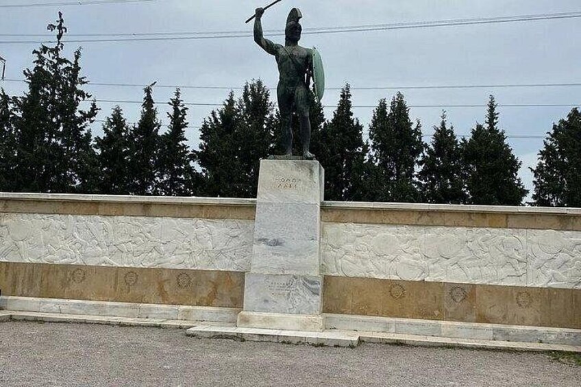 A statue of a figure holding a spear on a pedestal, with a stone wall and trees in the background. 4