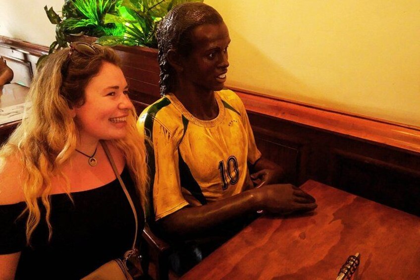 Twee personen zitten aan een houten tafel in een restaurant, met een plant op de achtergrond. 4