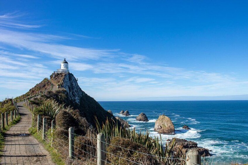 Un sentier côtier menant à un phare, des affleurements rocheux et l’océan. 1
