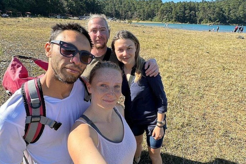 Un grupo de personas tomándose un selfie en un campo de hierba con un lago al fondo. 1