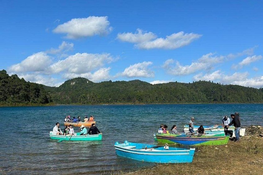 Un lago con barcos, gente y una colina boscosa al fondo. 3