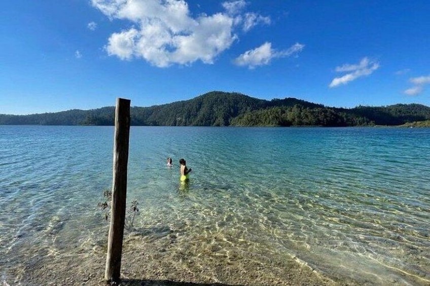 Un lago con aguas cristalinas, un poste de madera y una persona nadando. 4