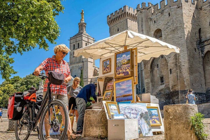 A person with a bicycle, a street vendor with paintings, and a castle in the background. 2