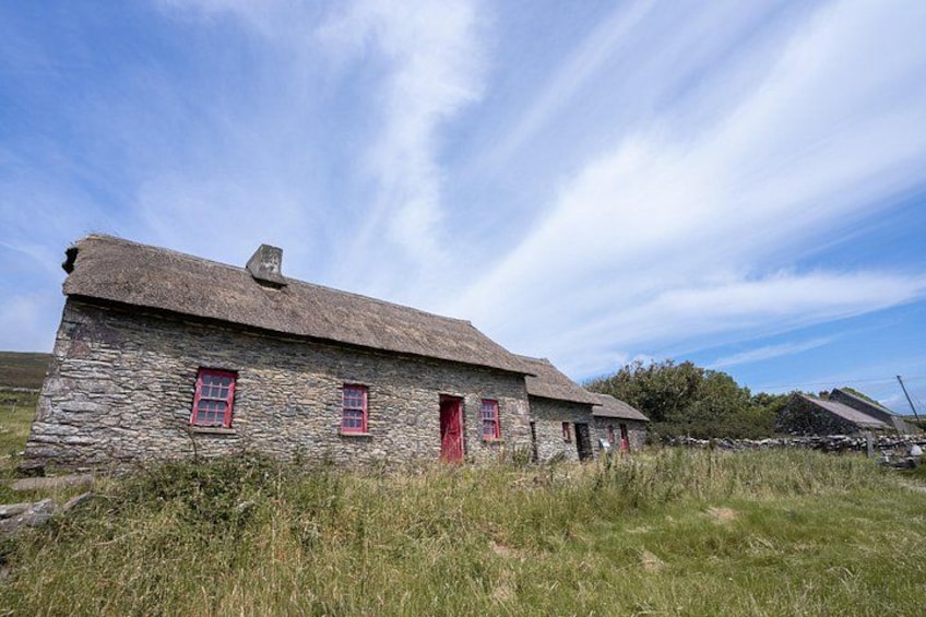 A stone house with a thatched roof, red doors, and windows, surrounded by grass and a clear sky. 2