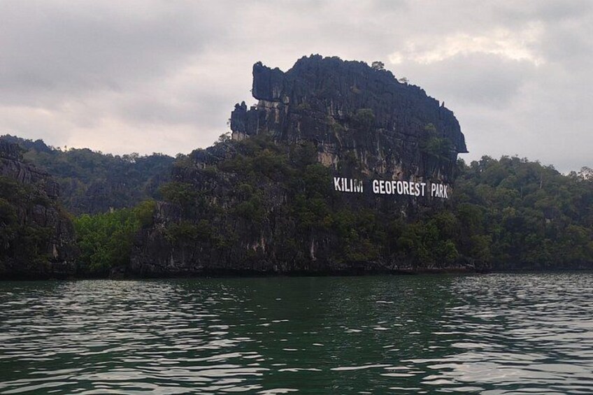 Une grande formation rocheuse sur laquelle on peut lire l’inscription « Kilimang Geoforest Park », entourée d’eau et de verdure. 3
