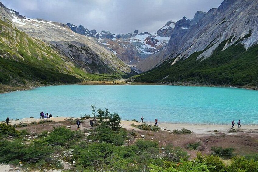 A turquoise lake surrounded by mountains, with people hiking around the area. 5