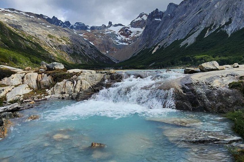 A mountain stream with clear water flowing over rocks, surrounded by rugged mountains and greenery. 4