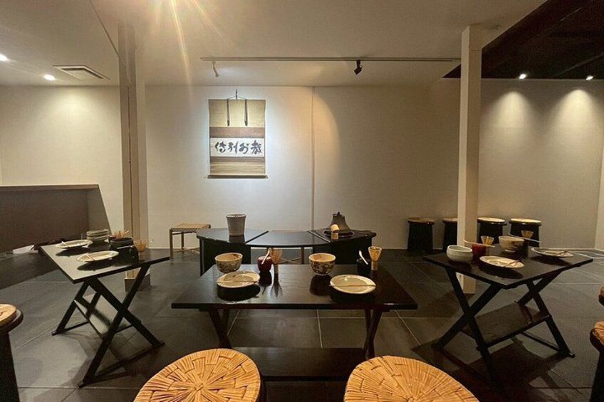 Een moderne eetruimte met donkerhouten tafels en stoelen, een centrale tafel met servies en een bord met Japanse tekens aan de muur. 4