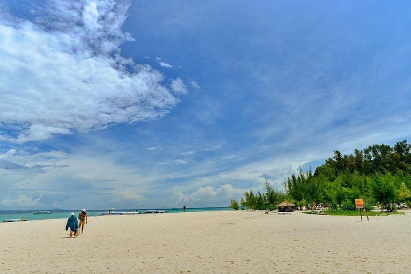 A beach with a clear sky, a few people walking, and some boats in the water. 5
