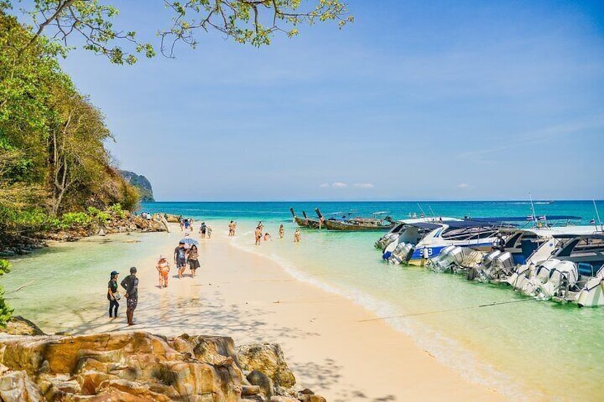 A beach with clear turquoise water, people walking, and boats parked on the shore. 3