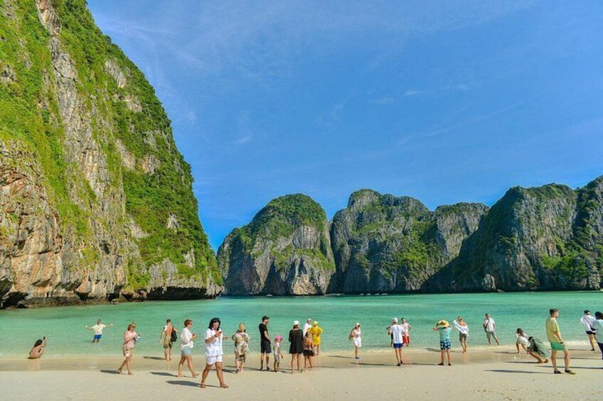 A beach with people walking, surrounded by green cliffs and clear turquoise water. 2