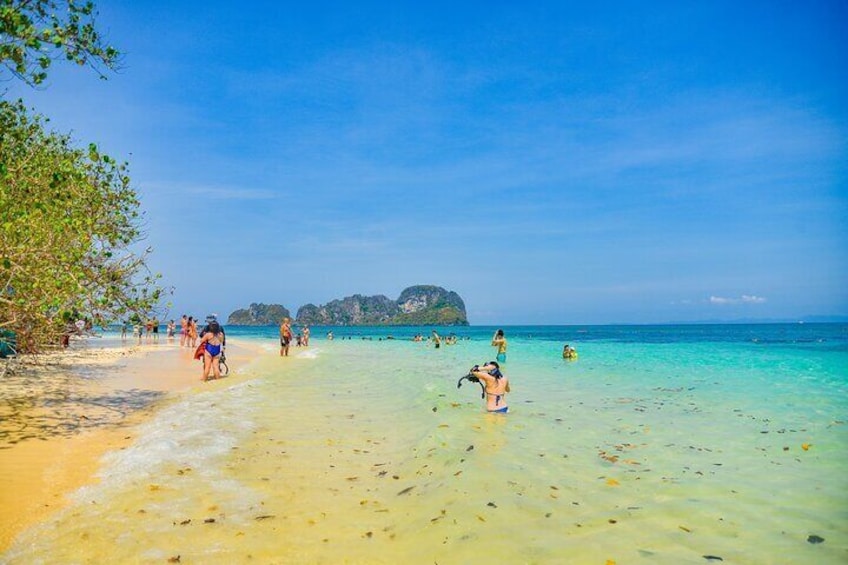 A beach with people swimming and walking along the shore, clear turquoise water, and a distant island. 4