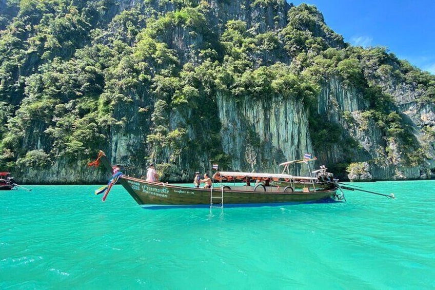 A long-tail boat on turquoise water with a forested cliff in the background. 1