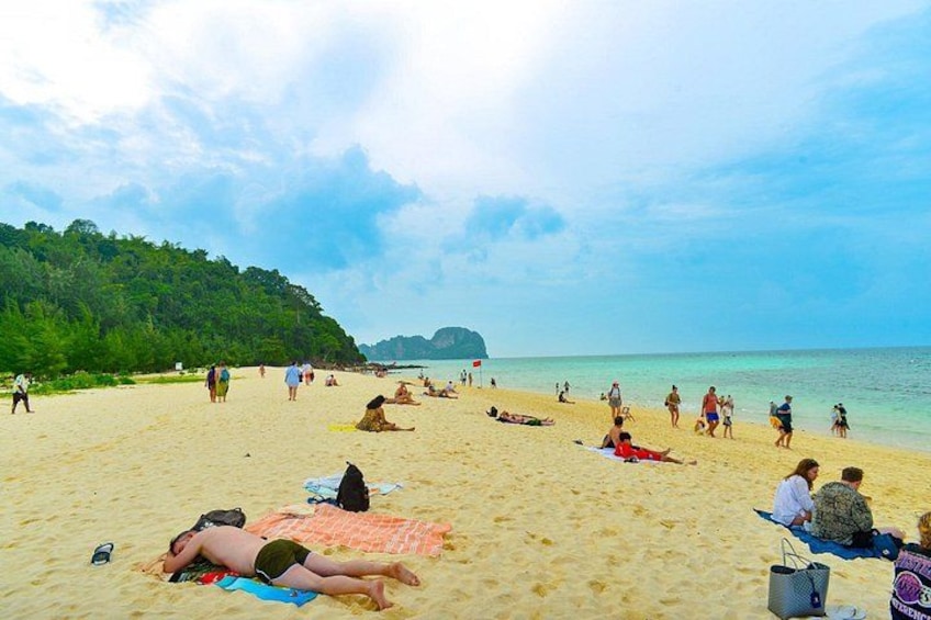 Une plage où l’on peut voir des gens se prélasser au soleil et se promener, un ciel dégagé et une colline boisée. 5