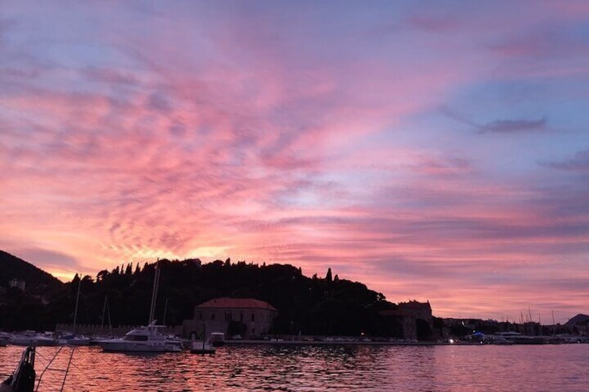 Un atardecer sobre una masa de agua con un edificio en una colina y barcos en primer plano. 1