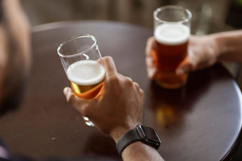 Two hands holding glasses of beer on a round table. 4