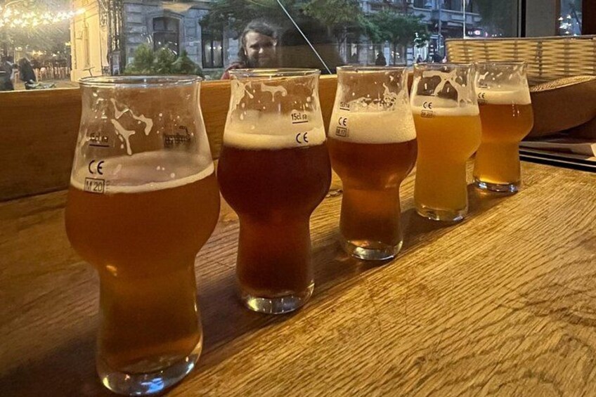 A row of five glasses of beer on a wooden table. 4
