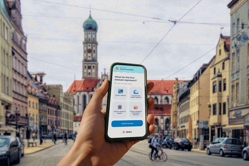 A hand holding a smartphone with a question about four statues on a street with buildings and a tower in the background. 1