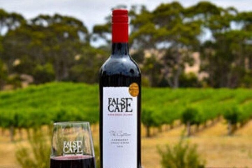 A bottle of wine and a glass with the label 'FALSE CAPE' in a vineyard setting. 4