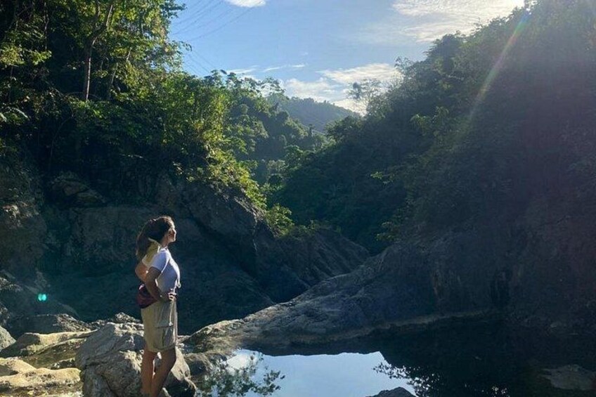 A person standing on a rocky outcrop overlooking a valley with a body of water and dense greenery. 3