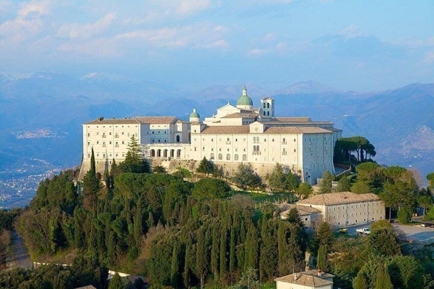 A large white building with domes, surrounded by trees and mountains in the background. 1