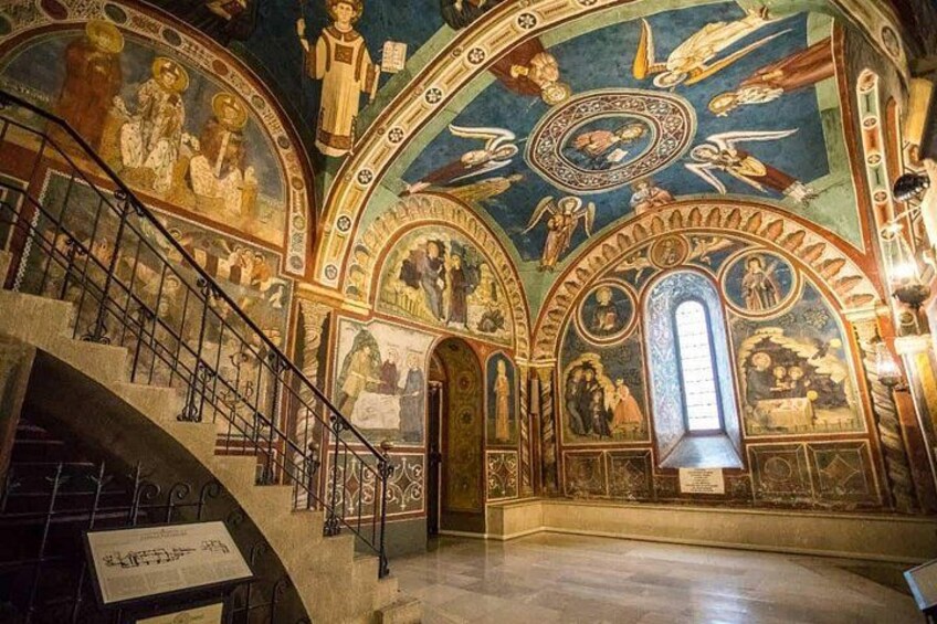 A grand hall with ornate frescoes, a staircase, and a large arched window. 2
