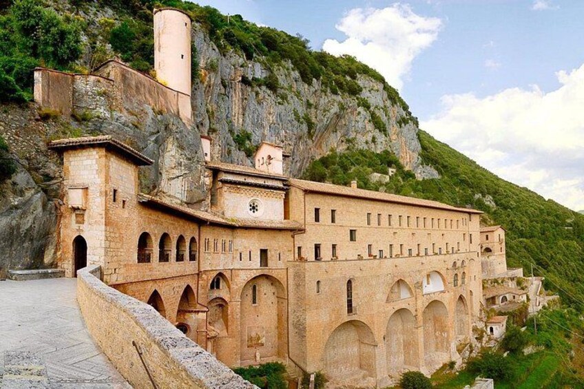 A historic building with arched windows and a bell tower, situated on a hillside with a rocky backdrop. 3
