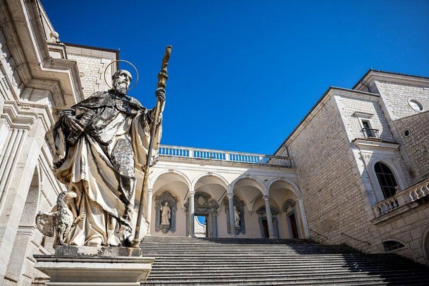 A statue on a pedestal, a building with arches, and a clear blue sky. 4