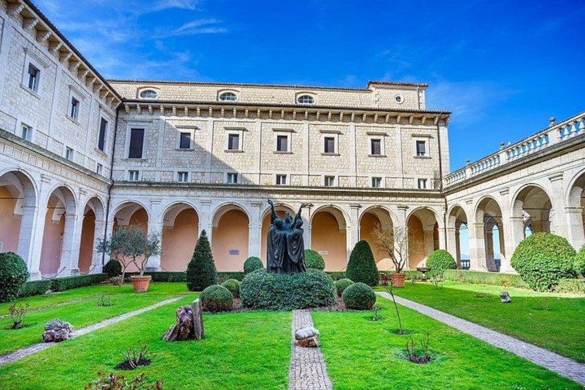 A courtyard with a statue, a building with arches, and well-maintained greenery. 2