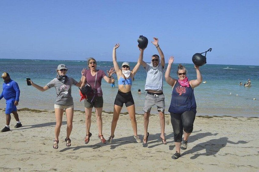 A group of people on a beach, some holding helmets, with the ocean and clear sky in the background. 3