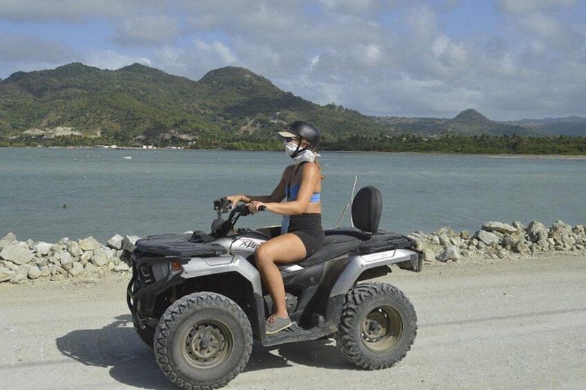 A person riding an ATV on a paved path near a body of water with mountains in the background. 2
