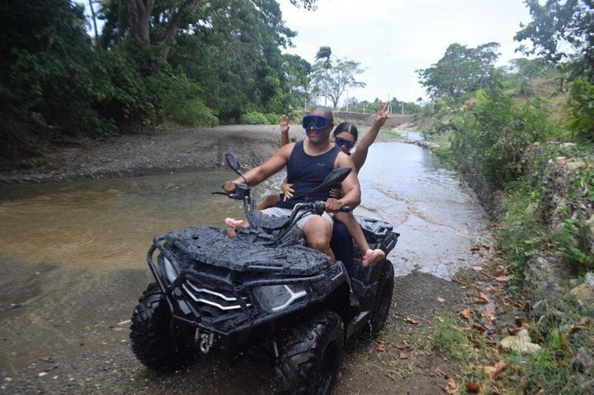 A person riding an ATV on a muddy path beside a waterway. 4