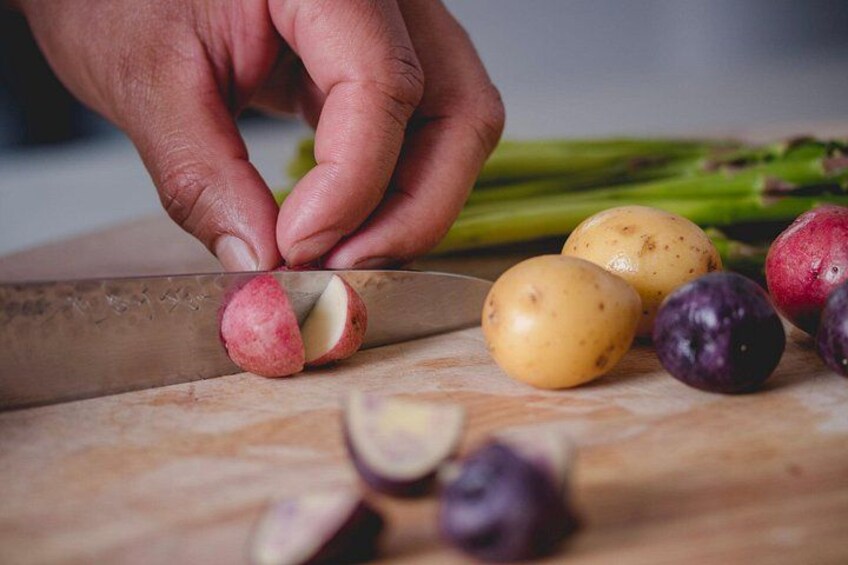 A hand slicing a red potato on a wooden cutting board with other potatoes and an onion nearby. 3