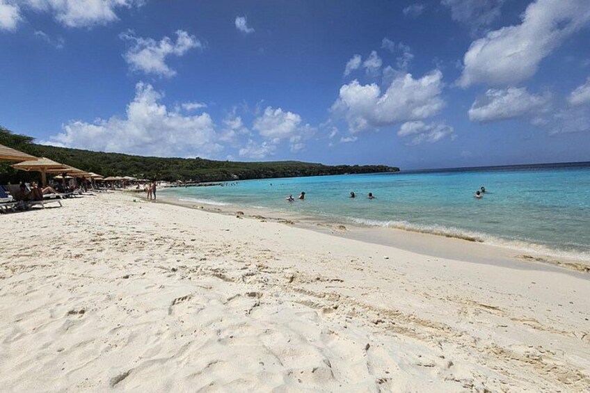 Una playa con arena blanca, agua turquesa cristalina y algunas personas nadando. 2
