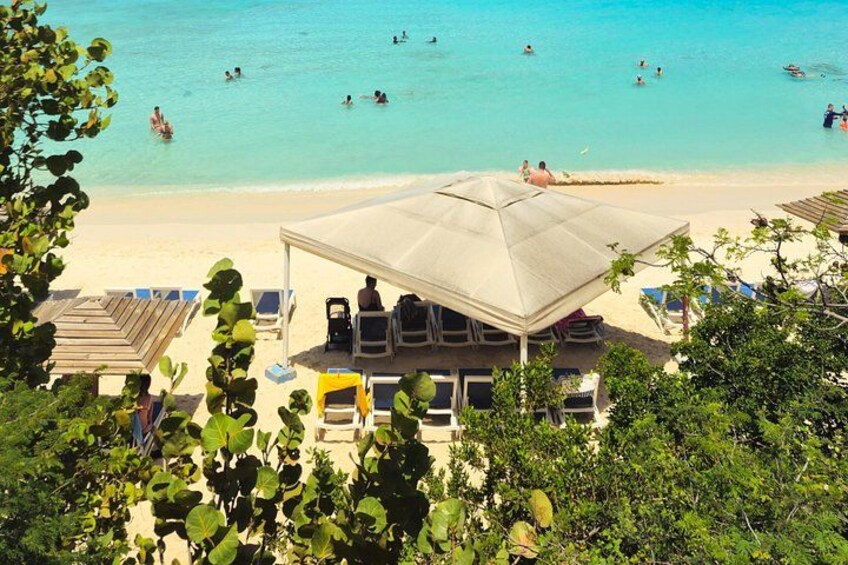 Una playa con gente nadando, una zona de estar cubierta y exuberante vegetación. 3