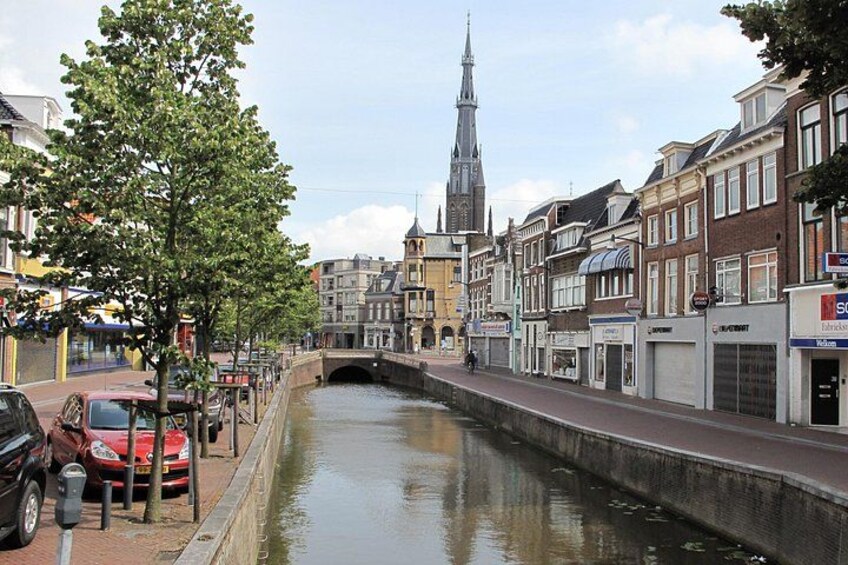 A canal with buildings on one side and a church spire in the background. 2