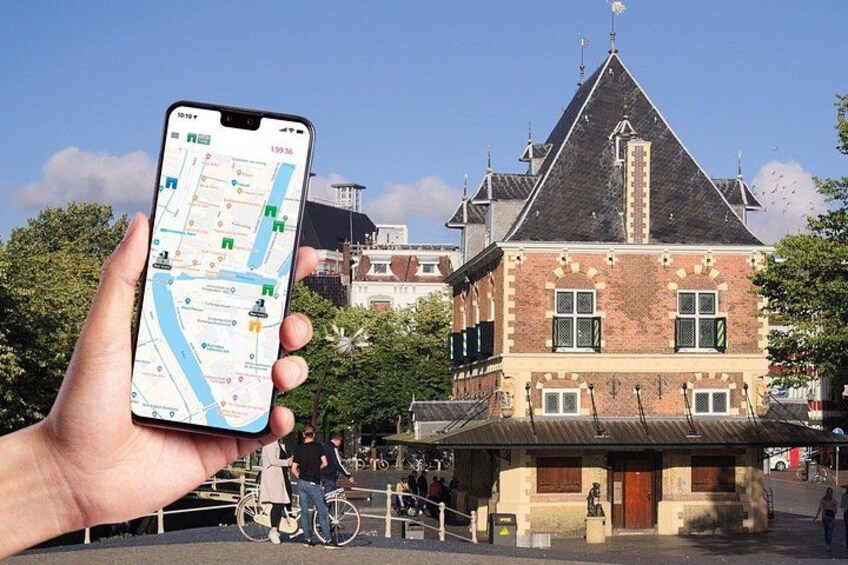 A hand holding a smartphone with a map application, a historic building with a steep roof, and a bicycle in the foreground. 1
